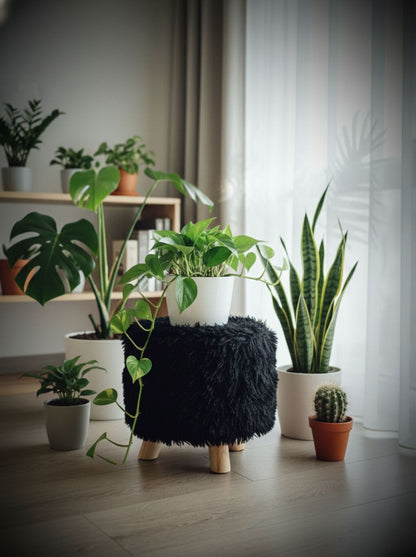 Puff negro peludo en ambiente con plantas, patas de madera natural